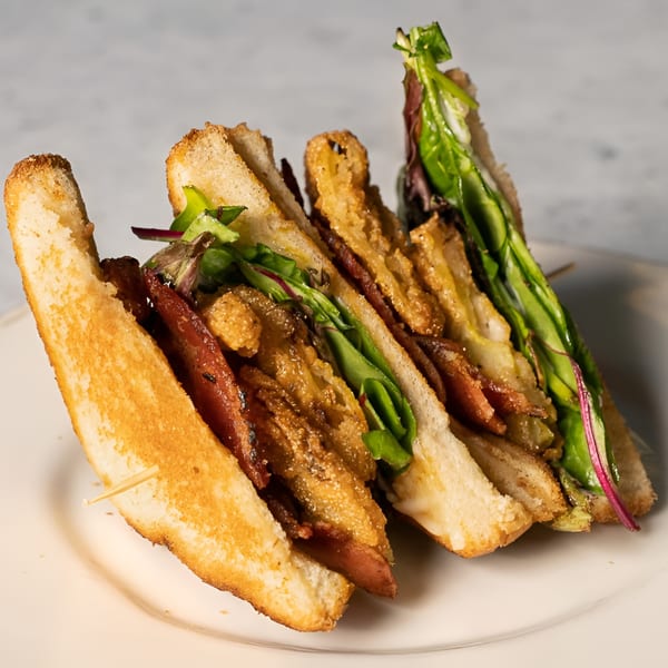A club sandwich with bacon, fried oysters, and greens, cut into triangles on a white plate.