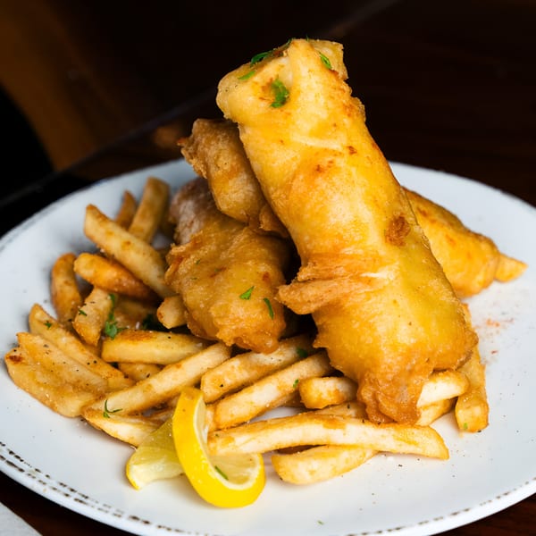 Golden-brown fish and chips with a lemon wedge and parsley on a white plate at 412 Public House.