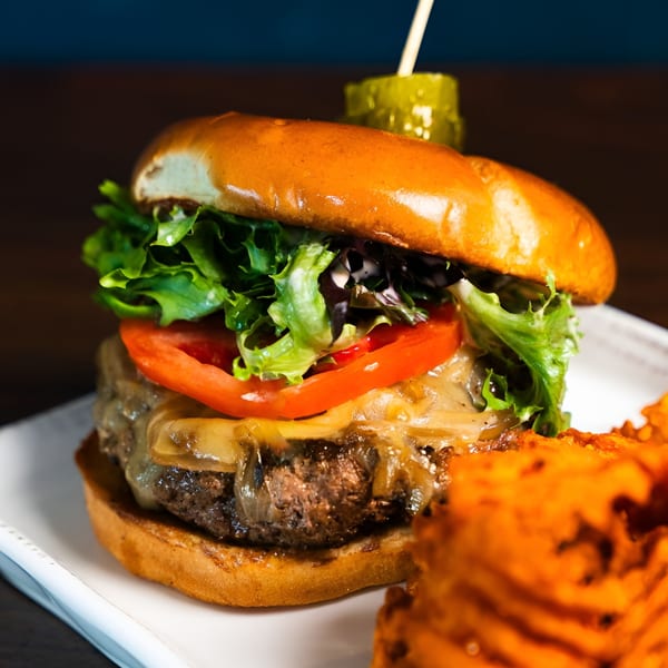 A juicy burger with melted cheese, lettuce, tomato, and caramelized onions, served with sweet potato fries.