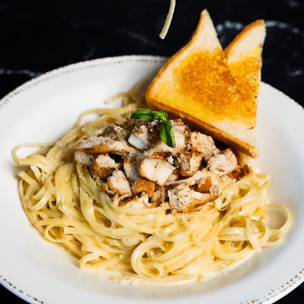 Chicken Alfredo pasta with a sprig of basil, parmesan, and two slices of Texas toast.